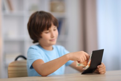 Photo of Boy with pocket money at wooden table indoors, selective focus