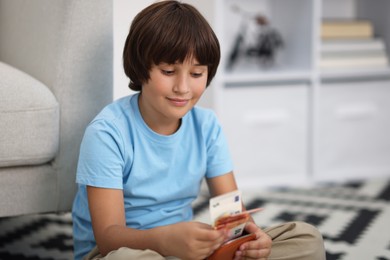 Photo of Boy with pocket money on floor at home. Space for text