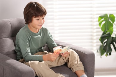 Photo of Boy with pocket money in armchair at home. Space for text