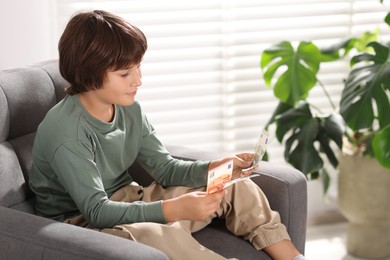 Photo of Boy with pocket money in armchair at home. Space for text