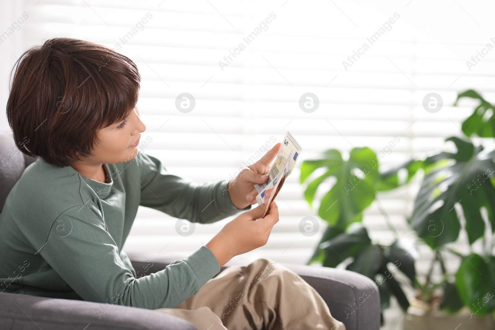 Photo of Boy with pocket money in armchair at home. Space for text