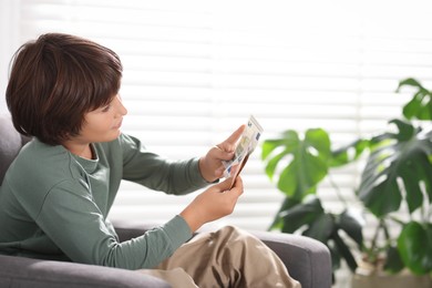 Photo of Boy with pocket money in armchair at home. Space for text
