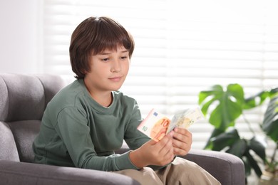 Photo of Boy with pocket money in armchair at home. Space for text