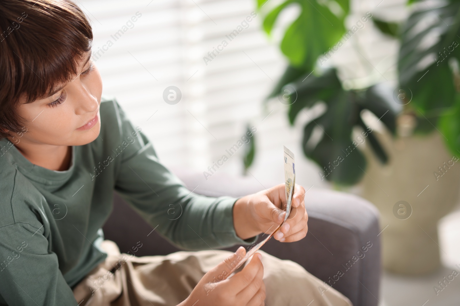 Photo of Boy with pocket money in armchair at home. Space for text