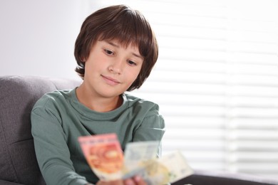 Photo of Boy with pocket money in armchair at home. Space for text