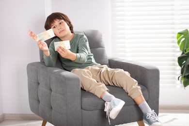 Photo of Boy with pocket money in armchair at home