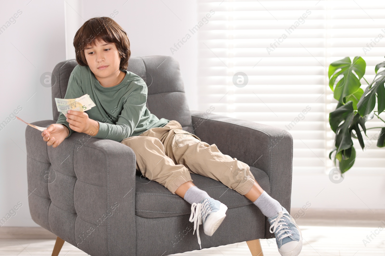 Photo of Boy with pocket money in armchair at home. Space for text