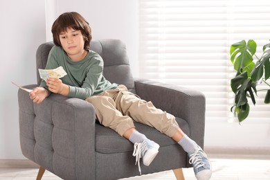 Photo of Boy with pocket money in armchair at home. Space for text