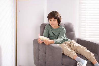 Photo of Boy with pocket money in armchair at home. Space for text