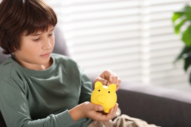 Photo of Boy putting his pocket money into piggy bank in armchair at home. Space for text
