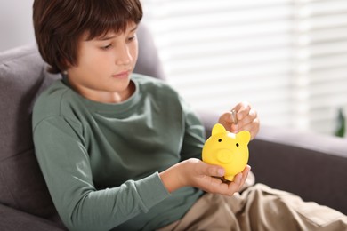 Photo of Boy putting his pocket money into piggy bank in armchair at home