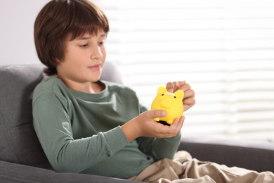 Photo of Boy putting his pocket money into piggy bank in armchair at home