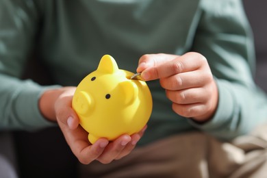 Photo of Boy putting his pocket money into piggy bank in armchair at home, closeup