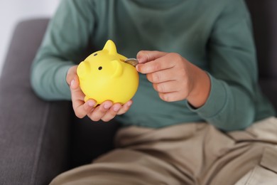 Photo of Boy putting his pocket money into piggy bank in armchair at home, closeup