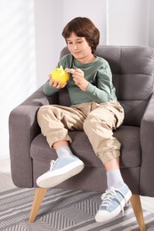 Photo of Boy putting his pocket money into piggy bank in armchair at home