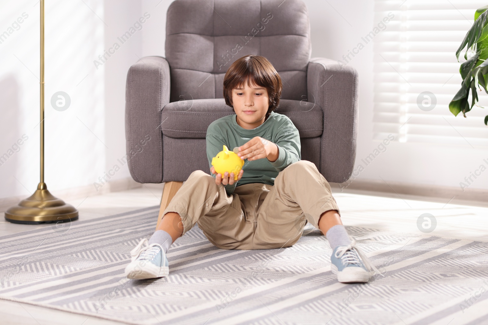 Photo of Boy putting his pocket money into piggy bank on floor at home