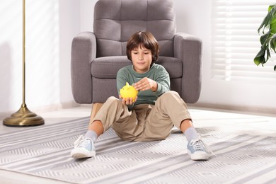 Photo of Boy putting his pocket money into piggy bank on floor at home