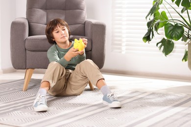 Photo of Boy putting his pocket money into piggy bank on floor at home. Space for text