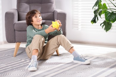 Photo of Boy putting his pocket money into piggy bank on floor at home. Space for text