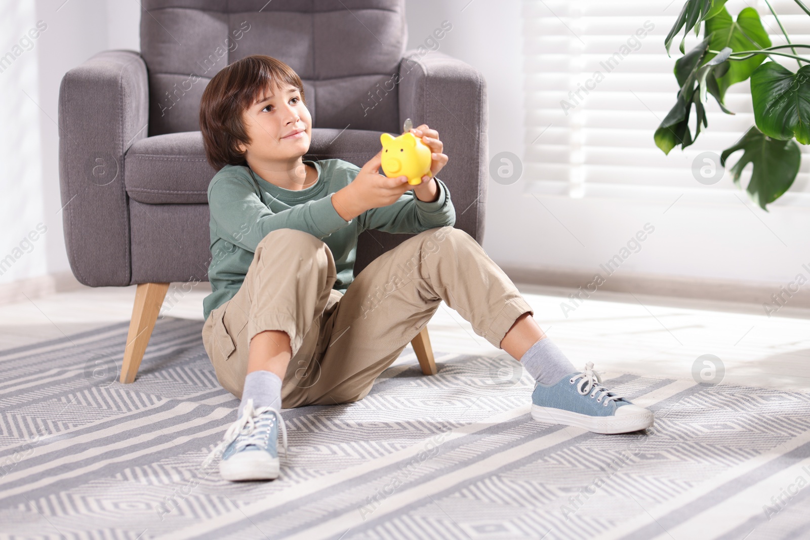 Photo of Boy putting his pocket money into piggy bank on floor at home