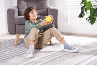 Photo of Boy putting his pocket money into piggy bank on floor at home