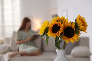 Photo of Girl reading book at home, focus on beautiful sunflowers in vase