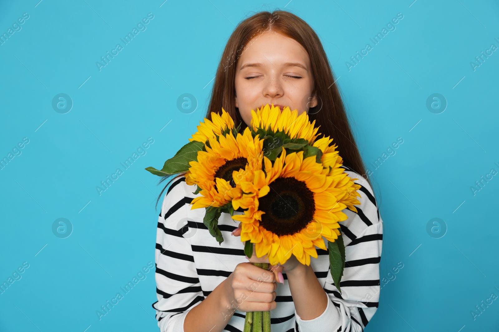 Photo of Teenage girl with bouquet of beautiful sunflowers on light blue background