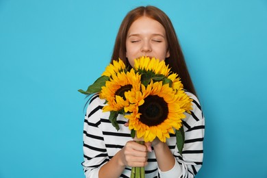 Photo of Teenage girl with bouquet of beautiful sunflowers on light blue background