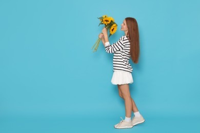 Photo of Teenage girl with bouquet of beautiful sunflowers on light blue background, space for text