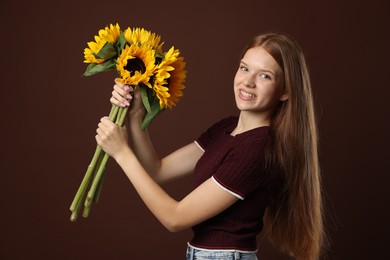 Photo of Teenage girl with bouquet of beautiful sunflowers on brown background