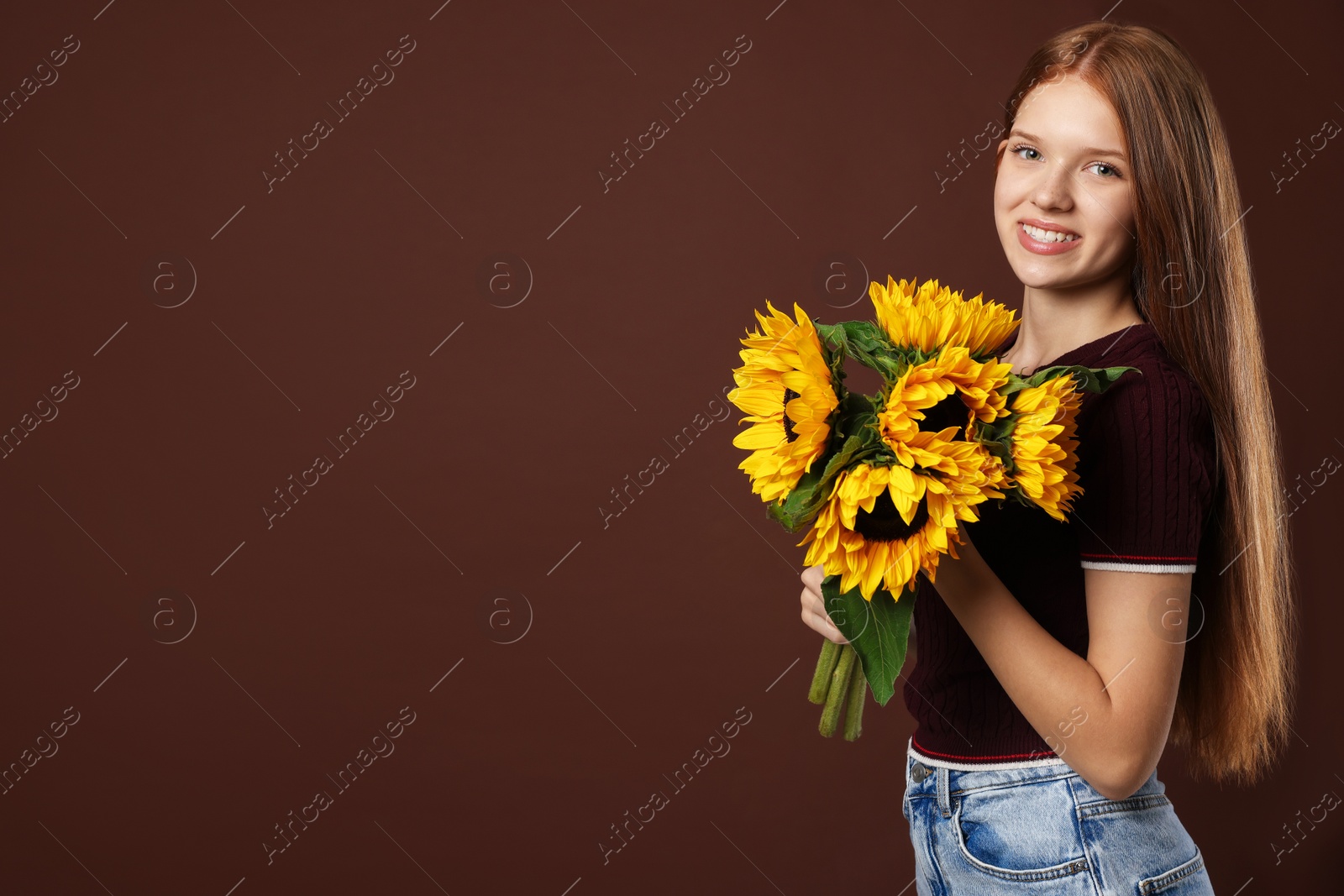 Photo of Teenage girl with bouquet of beautiful sunflowers on brown background, space for text