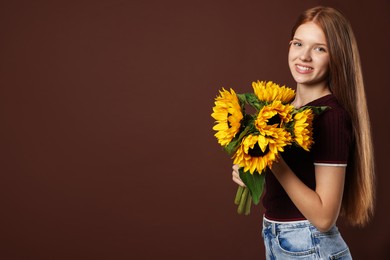Photo of Teenage girl with bouquet of beautiful sunflowers on brown background, space for text