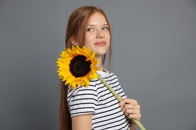 Photo of Teenage girl with beautiful sunflower on grey background