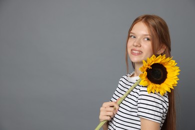 Photo of Teenage girl with beautiful sunflower on grey background, space for text