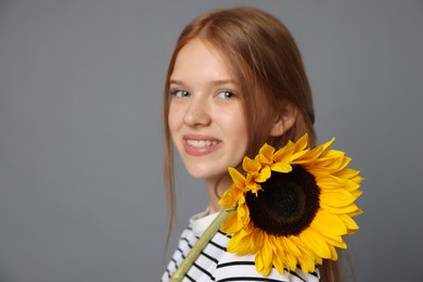 Photo of Teenage girl with beautiful sunflower on grey background, space for text