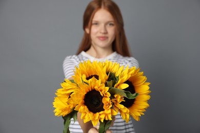 Photo of Teenage girl with bouquet of beautiful sunflowers on grey background, selective focus