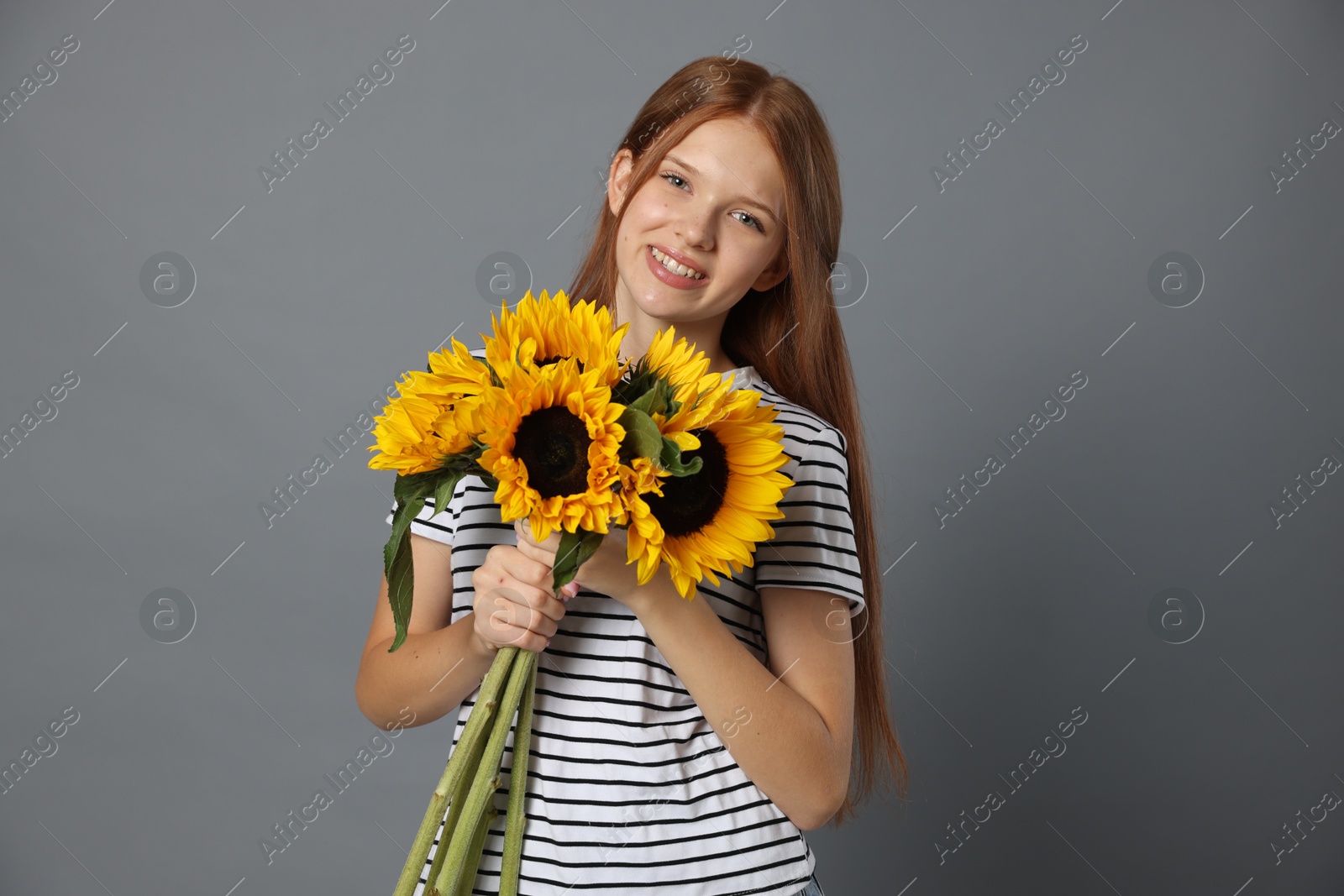 Photo of Teenage girl with bouquet of beautiful sunflowers on grey background