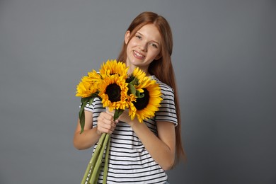 Photo of Teenage girl with bouquet of beautiful sunflowers on grey background