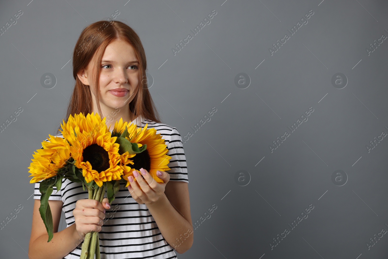 Photo of Teenage girl with bouquet of beautiful sunflowers on grey background, space for text