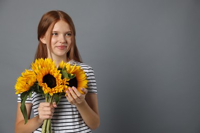 Photo of Teenage girl with bouquet of beautiful sunflowers on grey background, space for text