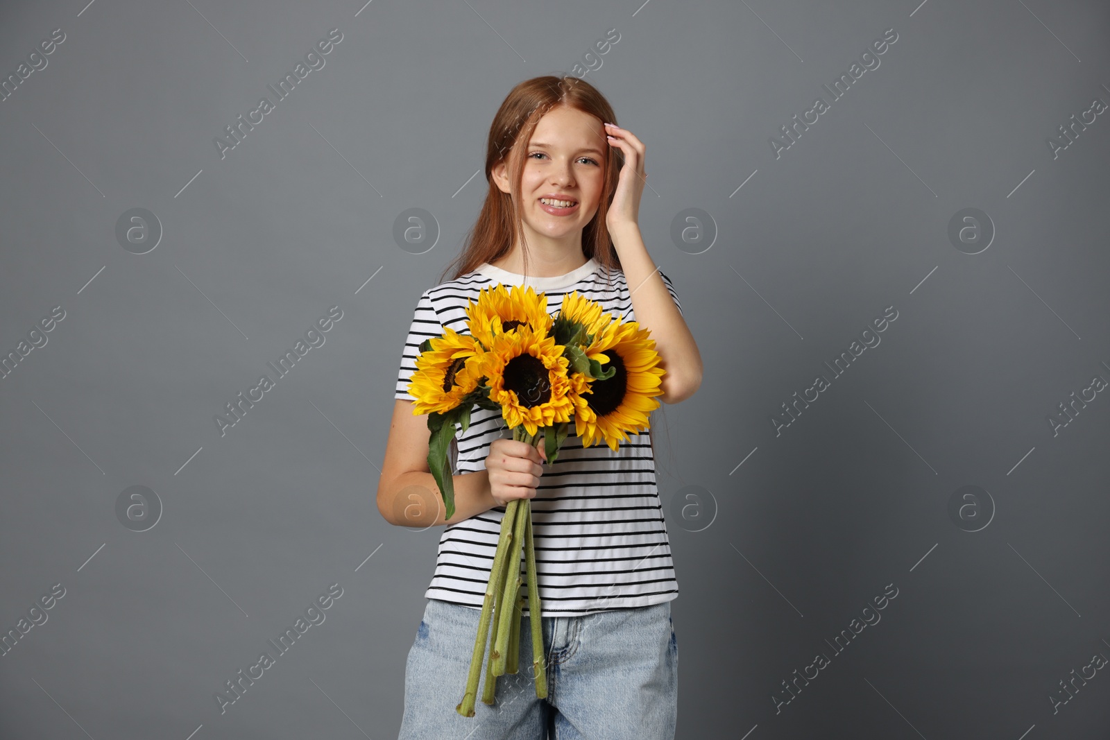 Photo of Teenage girl with bouquet of beautiful sunflowers on grey background