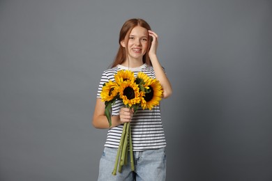 Photo of Teenage girl with bouquet of beautiful sunflowers on grey background