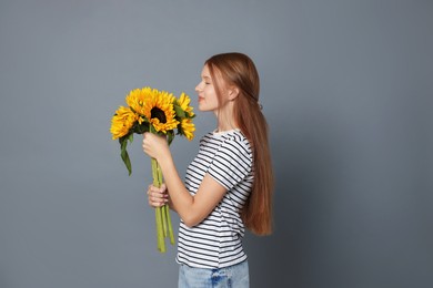 Photo of Teenage girl with bouquet of beautiful sunflowers on grey background
