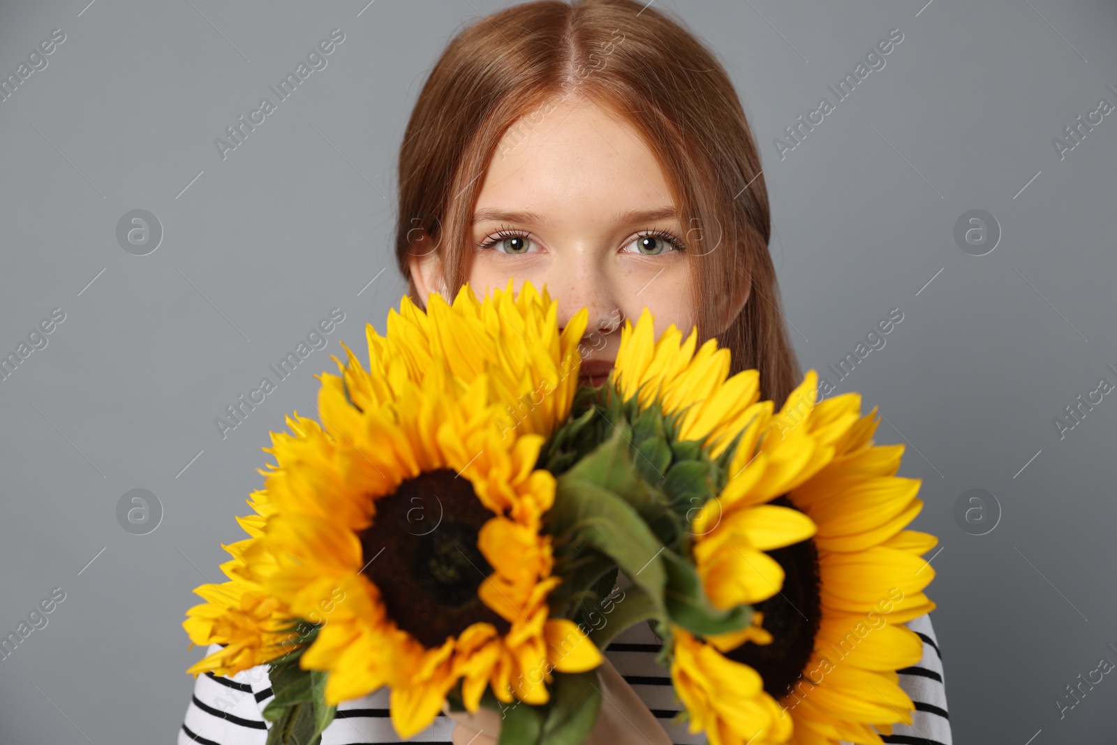 Photo of Teenage girl with bouquet of beautiful sunflowers on grey background