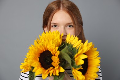 Photo of Teenage girl with bouquet of beautiful sunflowers on grey background