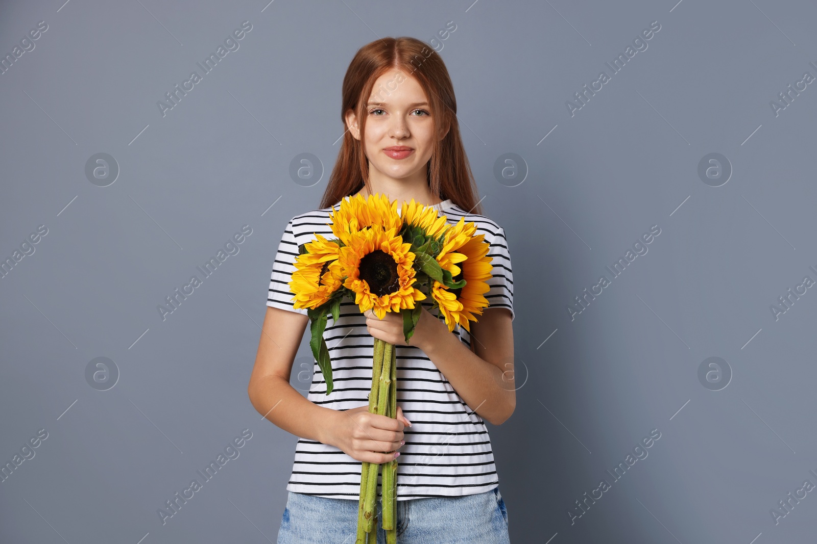 Photo of Teenage girl with bouquet of beautiful sunflowers on grey background