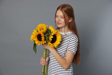 Photo of Teenage girl with bouquet of beautiful sunflowers on grey background