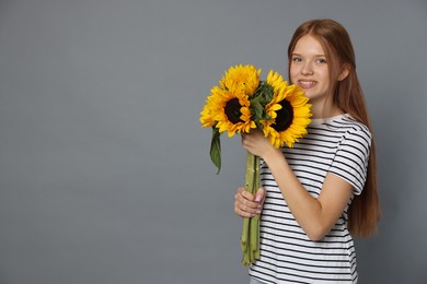 Photo of Teenage girl with bouquet of beautiful sunflowers on grey background, space for text