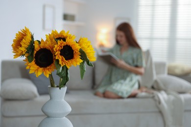 Photo of Girl reading book at home, focus on beautiful sunflowers in vase