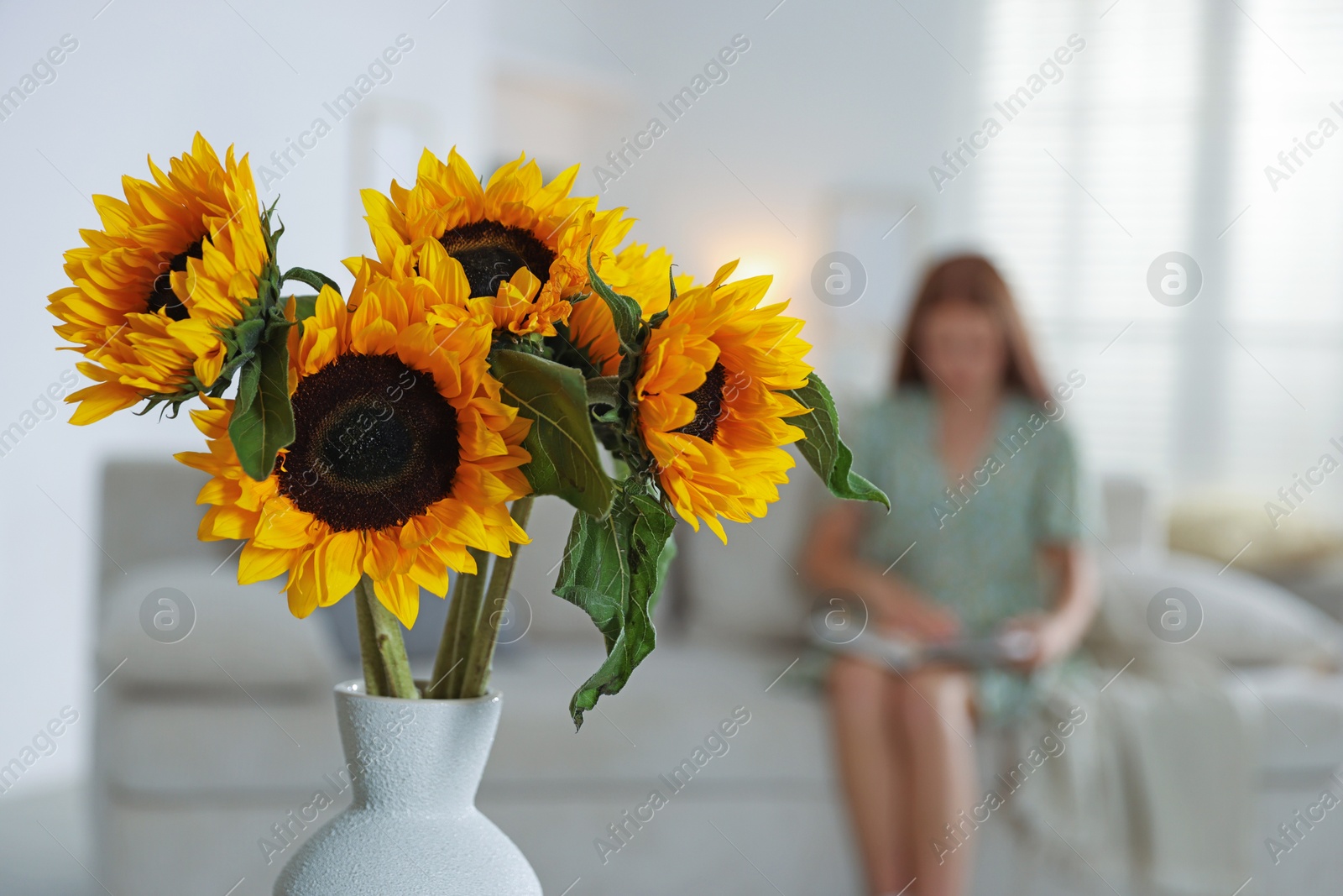 Photo of Girl reading book at home, focus on beautiful sunflowers in vase